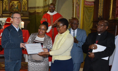 Oberbürgermeister Klaus Mohrs (links) überreicht die Urkunde zur Schulpartnerschaft an Schulleiterin Nombuso Mkhize (3.v.r.) in Anwesenheit von Bischof Pius Mlungisi Dlungwane (rechts). Foto: Stadt Wolfsburg