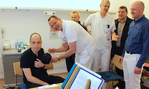 Dr. Thomas Hockertz nimmt die Impfung am stellvertretenden Stadtbrandmeister Marco Dickhut vor. Stadtbrandmeister Olaf Glaeske, Dr. Ulrich Heida, Geschäftsführer Axel Burghardt und Dr. Tobias Jüttner schauen ihm über die Schulter. Foto: Marian Hackert