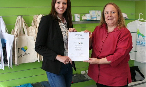 Stephanie Möller(links) und Susanne Große-Freese präsentieren die Urkunde der Qualitätsinitiative „Reisen für Alle“ in der Wolfsburger Tourist-Information. Foto: WMG Wolfsburg
