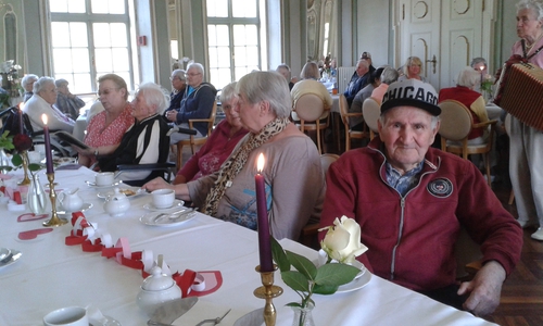 Blick in den Spiegelsaal der Seniorenbetreuung Schloß Schliestedt an die festlich gedeckten Muttertags-Kaffeetische mit selbstgebastelter Tischdekoration sowie im Hintergrund Frauenhilfemitglied Edith Belusa am Akkordeon in Aktion. Foto: privat