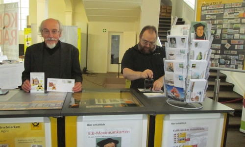 Dr. Benno Dalhoff aus Soest / NRW, Ideen- und Vorlagegeber für die Schmuckumschlag und der individuellen Briefmarke und Autor der Ausstellung „Das Kreuz von Tschernobyl und Fukushima“ am Sonderpostamt in der Trinitatiskirche in Wolfenbüttel zusammen mit dem Postbeamten Herrn Fode, der gerade den Sonderstempel auf einen Schmuckumschlag aufbringt. Foto: Privat