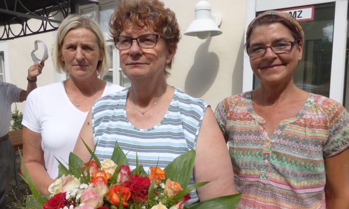 Die Dienstjubilarin Carola Ühre (Mitte) mit Blumenpräsent und zwei ihrer Kolleginnen vorm „Langhaus“ der Seniorenbetreuung Schloß Schliestedt. Foto: Seniorenbetreuung Schloß Schliestedt