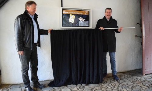 Sponsor Jürgen Breiler, Geschäftsführer der Firma Expert Riedel und Neumann, (links) und Oberbürgermeister Dr. Oliver Junk enthüllen den neuen Info- Bildschirm im Tordurchgang zum Großen Heiligen Kreuz. Foto: Stadt Goslar