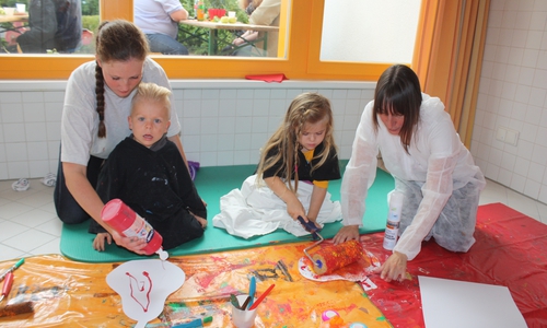 Im Matschraum des Kindergartens durften die Kinder nach Lust und Laune
mit Farben hantieren. Hier bemalen die Erzieherinnen Annika Bosse
(links) und Kerstin Drygall mit Tjard (zweiter von links) und Tanee aus
Papier ausgeschnittene Äpfel. Foto: Privat