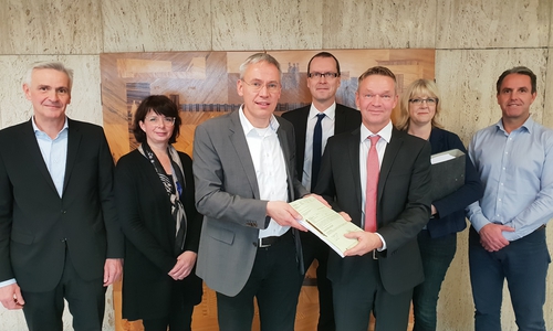Stadtbaurat Kai-Uwe Hirschheide (dritter von links) übergibt die Baugenehmigung an Marco Meyer (Buhlmann Immobilien, dritter von rechts). Foto: Stadt Wolfsburg.