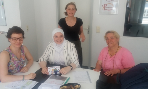 Hibatuallah Alzeer (Mitte sitzend) hilft ehrenamtlich Roveida Khomsi (rechts) im Alltag und bei der deutschen Sprache. Steffi Elena Bischoff (sehend) und Madeleine Martin (links) als Projektverantwortliche des Projektes „Frauenpower“ unterstützen dabei. Foto: Freiwilligenagentur Jugend-Soziales-Sport e.V. 