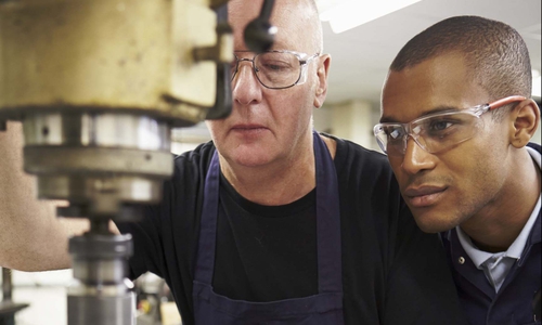 Ingenieur lehrt Azubi am Einsatz einer Fräsmaschine. Foto: Bundesagentur für Arbeit