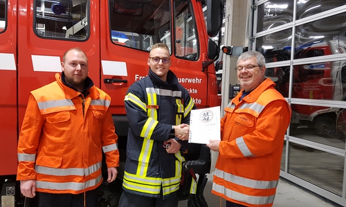 André Kohaupt und Andreas Bode gratulieren dem Hauptfeuerwehrmann Paul Gburek 