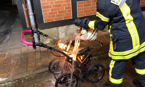 Ein Feuerwehrmann löscht den noch brennenden Kinderwagen.