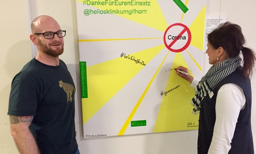 Nils Adam mit einer Mitarbeiterin vor seinem Corona Kunstwerk.