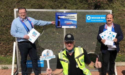 Schulleiter Klaus Scheller neben dem Schild, Günter Koschig mit dem neuen Präventionsmaterial des Weissen Ringes für die Sekundarstufen I und II und Martin Schilff mit der Zivilcouragekelle. 