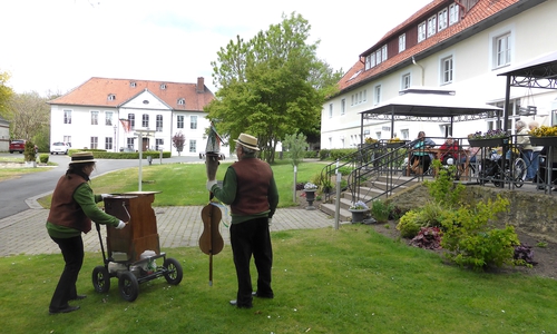 Die Drehorgelspieler vor dem Langhaus zur Freude der Bewohner. Im Hintergrund der Maibaum mit wehenden bunten Bändern vor dem Schlossportal.