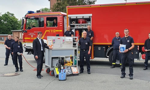Spendenübergabe Sparkassen-Regionalleiter Jens Müller (links neben dem Rollcontainer Hygiene) und Ortsbrandmeister Udo Löprich (rechts) mit Ausbildern und der Gruppe 1 bei der ersten Ausbildung zum Hygienekonzept.