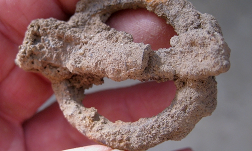 Früh- bis hochmittelalterliche ringförmige eiserne Gürtelschnalle in unrestauriertem Grabungszustand. Unten deutet sich eine Verzierung an.