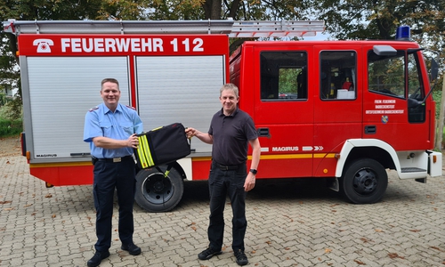 Schornsteinfegermeister Sven Holze (rechts) überreicht den Schornsteinfegerrucksack an einen Vertreter der Feuerwehr. 