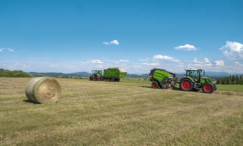 Traktoren mit einem Ladewagen (hinten) und einer Heuballenpresse. 