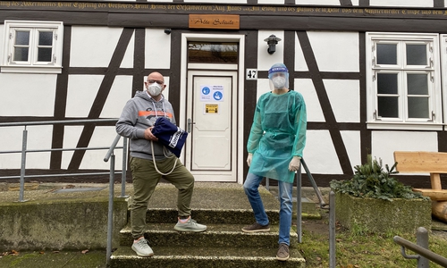 Ortsbürgermeister Marc Angerstein (li.) überreicht dem Fümmelser Teststellen-Betreiber ein Präsent zum Start des Testangebotes in der „Alten Schule“. 