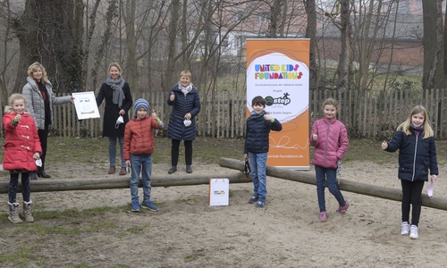 Claudia Kayser, Botschafterin des Kindernetzwerks United Kids Foundations und Leiterin der Direktion Wolfsburg bei der Volksbank BraWo (links), gratuliert jeweils einem Teil der im Wechselunterricht anwesenden Klasse 3n, Ulrike Svetlik (Schulleiterin) und Ute Schönian (Klassenlehrerin) zum Gewinn der 3. Bewegungschallenge und übergibt die Urkunde samt dem Preisgeld in Höhe von 150 Euro. 
