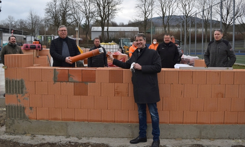 Oberbürgermeister Dr. Oliver Junk (vorn) und Burkhard Siebert, Erster Stadtrat und Fachbereichsleiter Bürgerservice (2. von links), bestücken die Zeitkapsel mit einer aktuellen Tageszeitung und einer Mund-und-Nasenmaske mit Goslar-Aufdruck. Zur Grundsteinlegung sind außerdem Giovanni Graziano als Vorsitzender des Ausschusses für Sicherheit, Ordnung und Sport (von links), Werner Penndorf, Vorstandsvorsitzender des Goslarer Sport Club von 1908 e.V., Maik Noack, Geschäftsführer der ausführenden Firma Noack Hoch- und Tiefbau GmbH & Co. KG, sowie Bauingenieur Markus Schmidt gekommen.