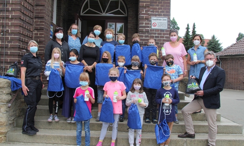 Schülerinnen und Schüler des Grundschule Oker nehmen symbolisch für die Kinder im Landkreis Goslar die Tüten in Empfang. Mit dabei ist die Rektorin der Grundschule Oker und ihre Kolleginnen, für die AG Gemeinsam gegen Gewalt Elke Ballhausen/Schulspezialdienst und Holger Fenker (stellvertretend für Claudia Hopp und Viktoria Osadtschi) Jugendschutz, beide vom Landkreis Goslar, Jenny Nemet vom Frauenhaus Goslar und Stephani Gobernack von der Polizeiinspektion Goslar. Es fehlt: Petra Franke, Koordinatorin Frühe Hilfen beim Landkreis Goslar. 