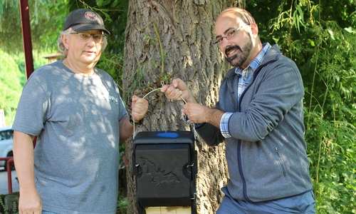 Ortsbrandmeister Bernhard Neumann (links) und Umweltingenieur Sven Glodniok (rechts) mit einem der neuen Fledermaus-Quartiere am Feuerwehrgerätehaus in Neuwallmoden. Hier wurden die 45 Kästen kurzzeitig gelagert, bis alle sicher an den markierten Positionen angebracht worden waren. Die Feuerwehr beherbergt in sicherer Höhe auch eines der neuen Fledermaus-Quartiere.