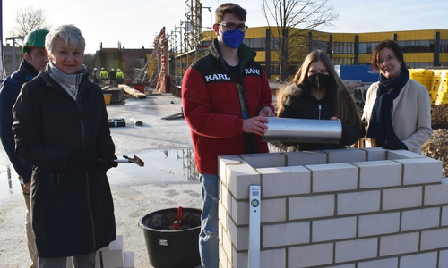 Die HBG-Schülerin Antonia Grüll und der HBG-Schüler Jason Holzberg legen zusammen mit Landrätin Christiana Steinbrügge (links) und Schulleiterin Katrin Unger (rechts) eine Zeitkapsel in den Grundstein.