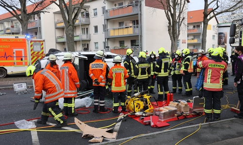 Einsatzkräfte vor dem aufgeschnittenen Fahrzeug, das in der Neißestraße auf der Seite liegt. Im Hintergrund (unkenntlich gemacht), ein Teil der zahlreichen Schaulustigen.