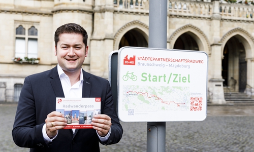 Oberbürgermeister Dr. Thorsten Kornblum mit dem Heft zum Radwanderpass am Start- und Zielpunkt des Städtepartnerschaftsradwegs vor dem Braunschweiger Rathaus.
