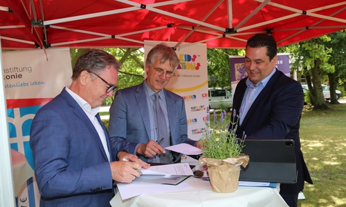 Thomas Fast (Volksbank BraWo Stiftung) und Dr. Jens Rannenberg (Dachstiftung Diakonie) unterzeichnen gegenseitig die Fördervereinbarung in Anwesenheit von Landrat Tobias Heilmann (v. li.).