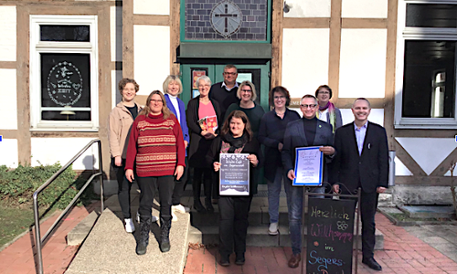 Von links: Marleen Wagener (Landkreis WF), Corinna Hoheisel (Landkreis WF), Sabine Walter (Leiterin Jugendamt WF), Petra Behrens-Schröter (Beauftragte für Diakonie WF/Salzgitter), Pfarrerin Stefanie Röber, Lars Dunkhorst (SG Elm-Asse), Andrea Föniger (Bürgermeisterin Schöppenstedt), Beate Maiberg (SG Elm-Asse), SGB Dirk Neumann, Bernd Retzki (Sozialdezernent Landkreis WF) und Sozialarbeiterin  Kerstin Hoffmann vor dem Eingang zum „SegensReich“. 