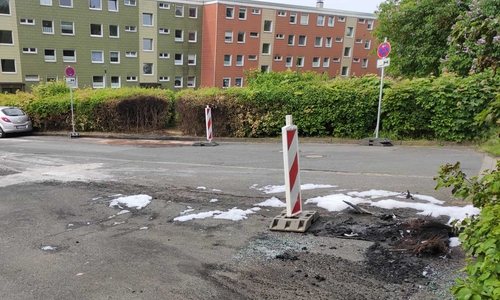 Der angesengte Asphalt zeugt vom nächtlichen Einsatz. Im Hintergrund sind noch die Spuren des ersten Fahrzeugbrandes zu sehen.