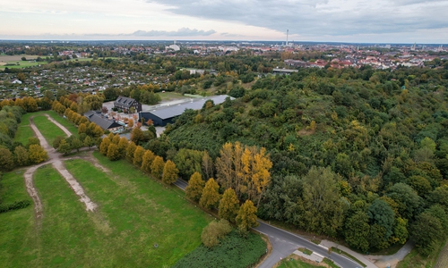 Links die Flächen, die bei Veranstaltungen zum Parken genutzt werden, obwohl es dafür keine Genehmigung gibt. Rechts der Milleniumberg und die Milleniumhalle.