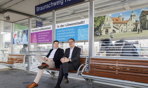 Oberbürgermeister Dr. Thorsten Kornblum und Gerold Leppa, Geschäftsführer des Stadtmarketings, präsentieren die neuen Beklebungen an den Sitzeinhausungen am Hauptbahnhof. 