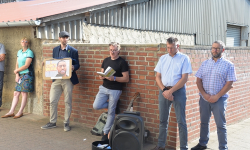 Im Beisein von Ratsmitgliedern, Landtagsabgeordneten und Bürgerinnen wie Bürgern gestalteten Ruben Herm (mit Plakat) von der AG MeGa, Lyriker Johann Voß (Mitte) und Jerxheims Bürgermeister Marko Hölz (Zweiter von rechts) die Stolperschwellen-Verlegung.