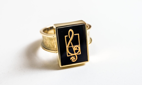 Die viereckige Fassung des Steins unterstreicht den klaren, modernen Charakter des Rings. Ein Notenschlüssel als Zeichen für musikalischen Ausdruck, ein Kleeblatt als Hinweis auf den Verleihungsort Hahnenklee sowie die Fibonacci-Spirale, die für Harmonie und das Streben nach Perfektion steht, ergänzen das gelungene Arrangement.