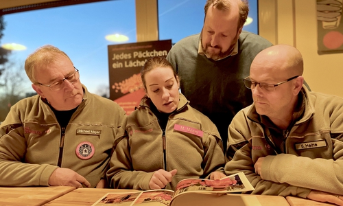 Michal Meyer, Maren Meers und die Regionalvorstände Heinrich von Bünau und Sven Heine gucken sich gemeinsam das Fotobuch voller Weihnachtstrucker-Erinnerungen an. 