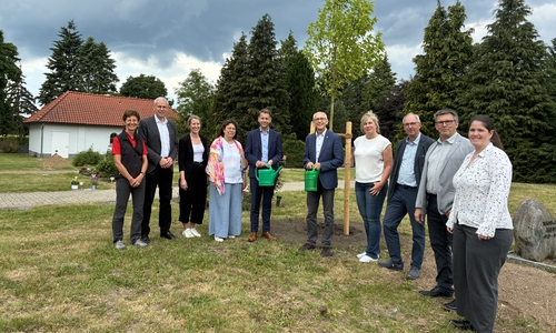 Mit einer symbolischen Baumpflanzung wurde die Übernahme des Friedhofsbetriebs in Neindorf durch die Stadt Wolfsburg zum 1. Juni 2026 sichtbar gemacht. Rund um den neu gepflanzten Baum versammelten sich Vertreterinnen und Vertreter aus Ortsrat, Stadtverwaltung und Kirche. Zu sehen sind unter anderem Oberbürgermeister Dennis Weilmann (Fünfter von links) und Superintendent Christian Berndt (Sechster von links).
