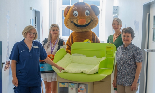 Das dm-Team um das Maskottchen SauBär übergab dem Team der Kinderchirurgie und -urologie des skbs sowie Chefärztin Dr. Andrea Schmedding (rechts) eine mobile Wickelstation.