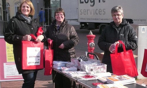 Birgit Grimm, Christine Scholz und Marion Meyer vom SoVD Kreisverband Gifhorn verteilen rote Taschen, die sinnbildlich auf die roten Zahlen in den Geldbörsen von Frauen hinweisen. Foto: SoVD Gifhorn.