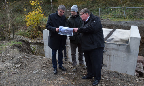 Wolfgang Lebzien (Mitte) zeigt Renke Droste (rechts) und Dr. Oliver Junk vor der neuen Brücke Fotos von den zerstörten Wegen in der Forst. Foto: Stadt Goslar