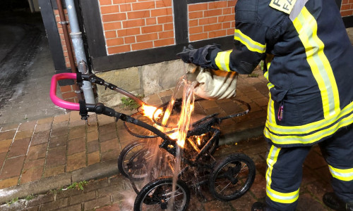 Ein Feuerwehrmann löscht den noch brennenden Kinderwagen.
