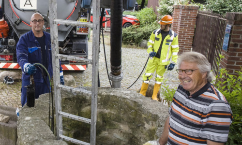Die SE|BS-Mitarbeiter Meik Krull (links) und Dominik von Zweydorff (im Hintergrund) reinigen den Mascheroder Brunnen – kein Problem mit der Spezialfahrzeugtechnik. Heimatpfleger Henning Habekost (rechts) freut sich über das Ergebnis.