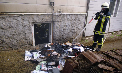Die Feuerwehr löscht die brennenden Materialien im Freien ab.