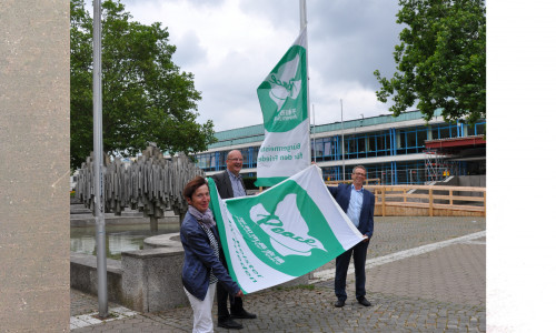 Klaus Mohrs, Bärbel Weist und Ingolf Viereck mit der "Mayors for Peace"-Flagge vor dem Wolfsburger Rathaus.