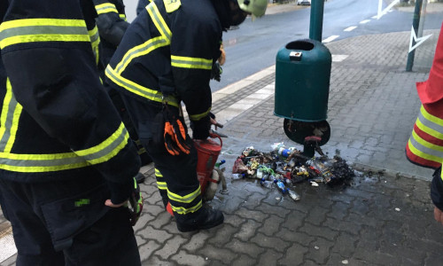 Die Feuerwehr löscht den brennenden Inhalt eines Abfalleimers mit einer Kübelspritze.
