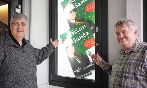 Chorleiter Andreas Lamken (links) und Kinobetreiber Harald Pape (rechts) präsentieren "Mission Santa" im Schaukasten des Roxy.