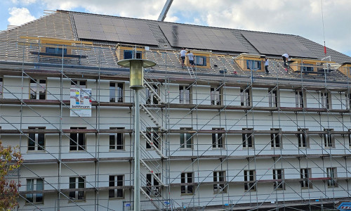 Das Gebäude erhält eine Photovoltaikanlage: Monteure arbeiten an der Installation der Module auf dem Dach.