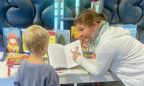 Sarina Nilsson zeigt Ben ein Buch von ihrem Büchertisch.