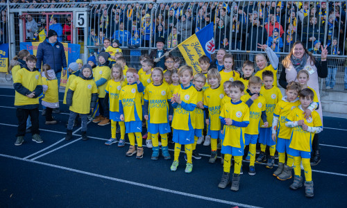 Ehemalige Frühgeborene posieren im Eintracht-Stadion mit gelben Einlaufshirts – ein besonderer Moment vor großem Publikum. 