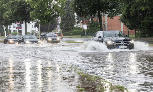 Mehrere Autofahrer fahren durch die überflutete Ludwig-Erhard-Straße.